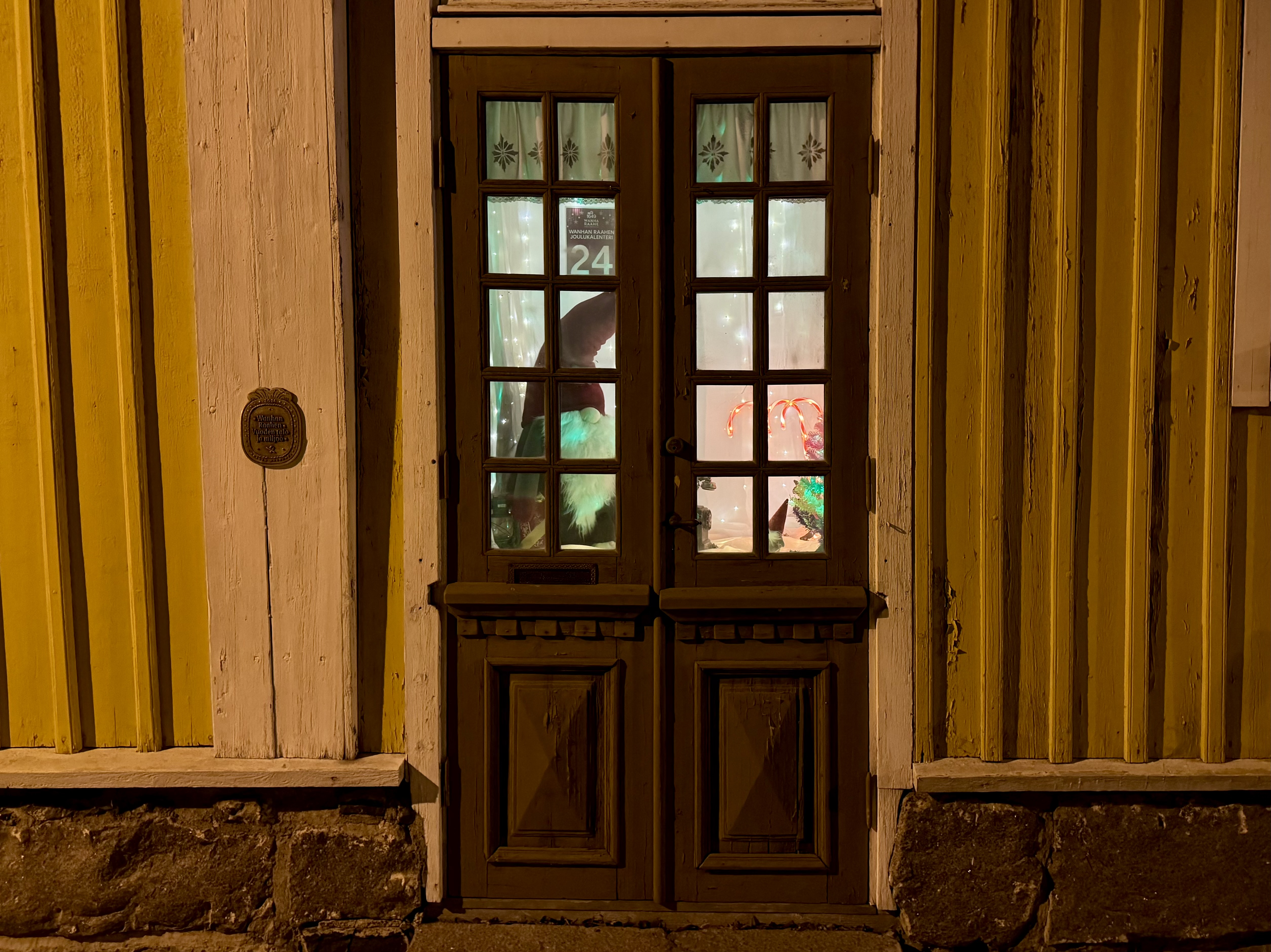 Luukku 24. Tonttu ja karkkiikeppejä ja valoja ikkunassa.