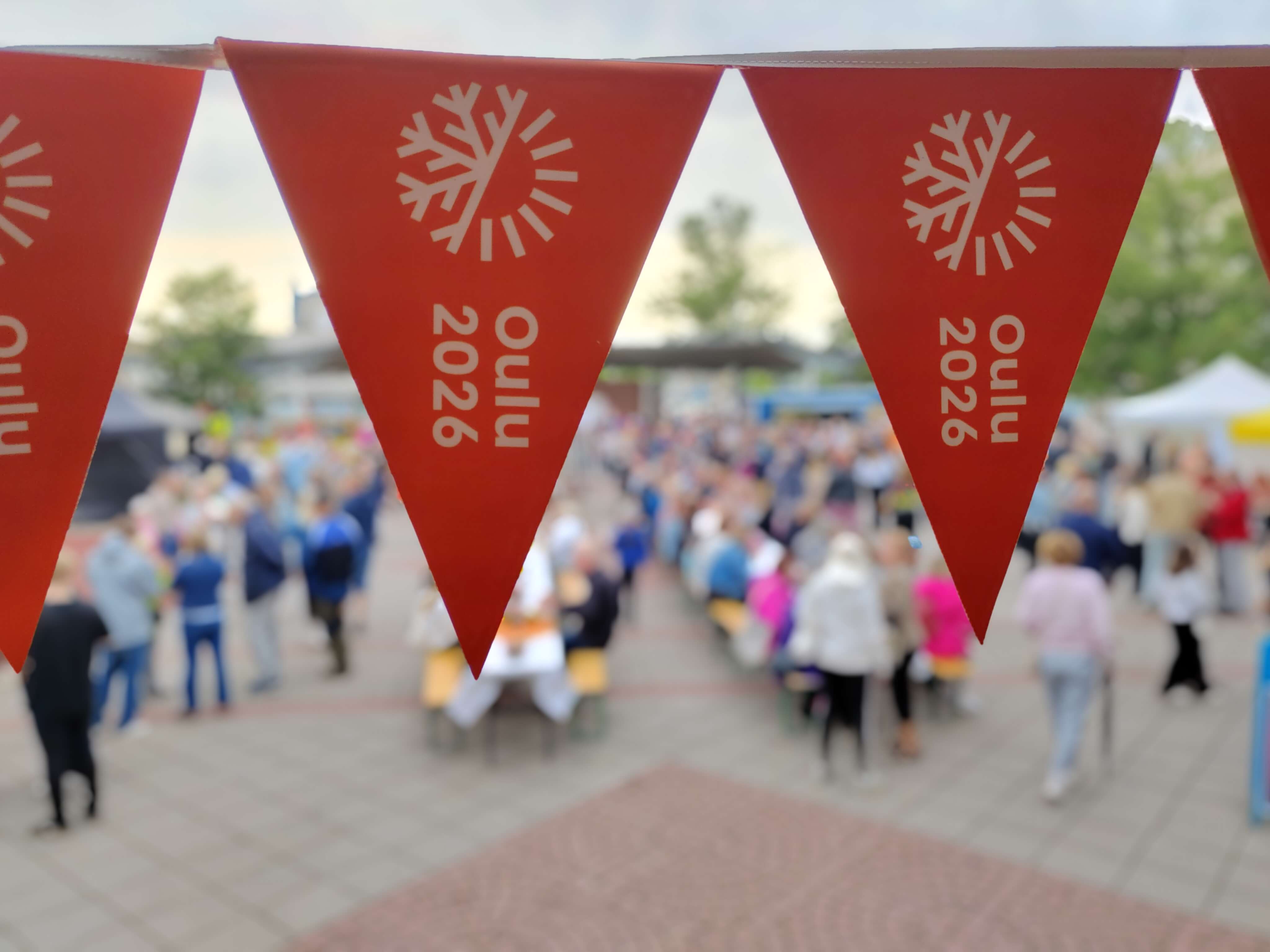 Oulu2026-viirejä, joiden takana näkyy runsaasti ihmisiä.