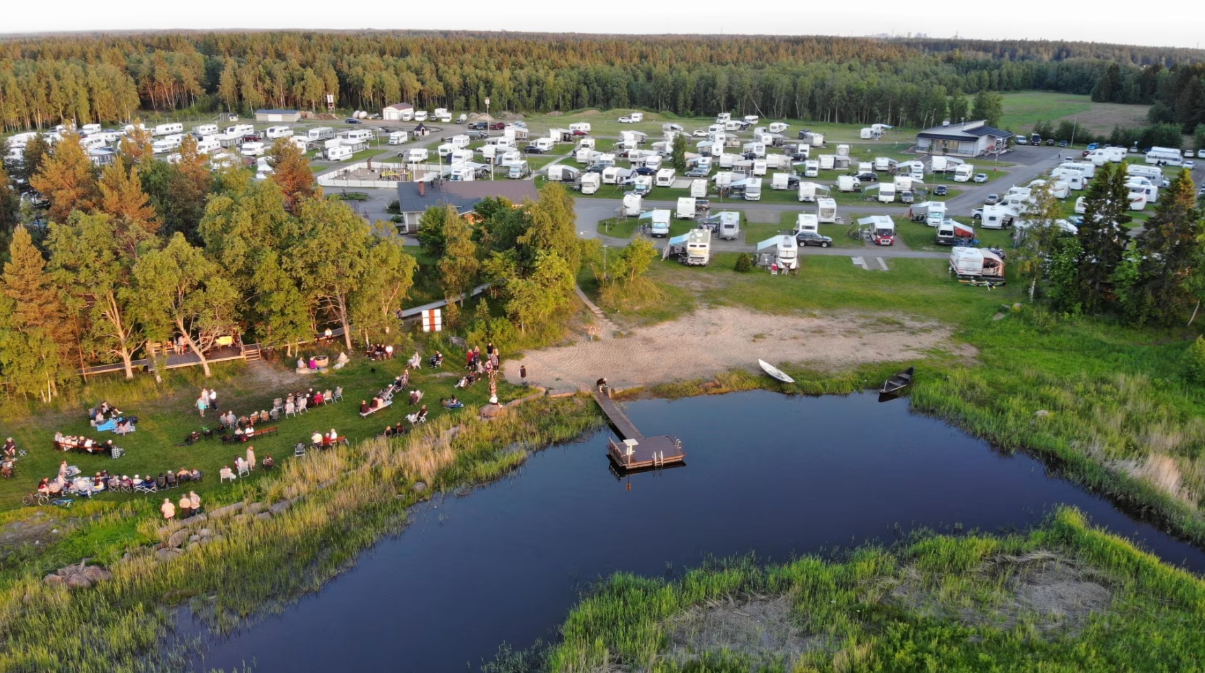Ilmakuva SF Caravan Lohenpyrstöstä merenrannalla. Paljon matkailuautoja parkissa, ihmiset kokoontuneet viettämään iltaa meren äärelle.