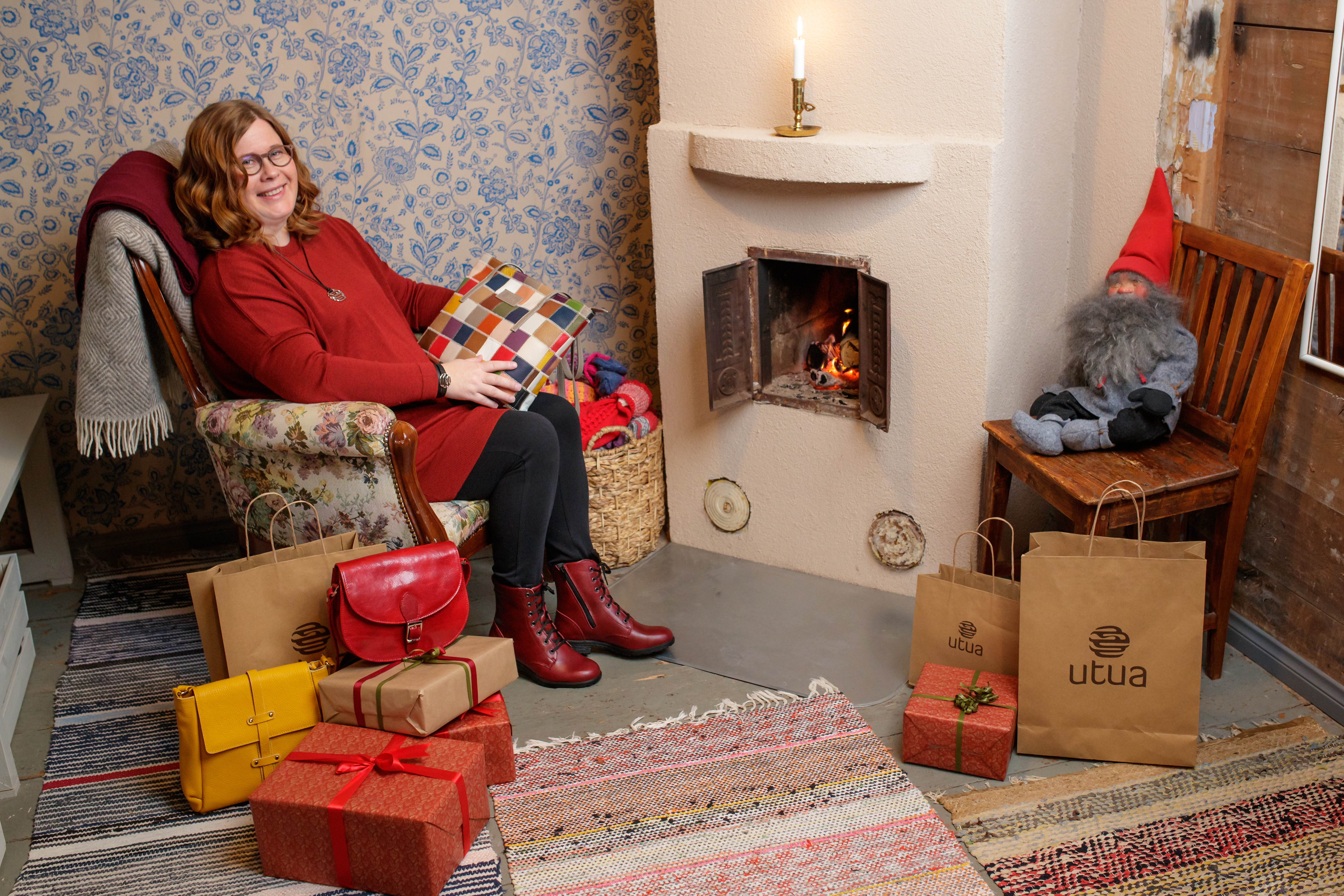 A person sitting next to a fireplace in a Christmas setting, presents on the floor, holding a leather bag in their hands