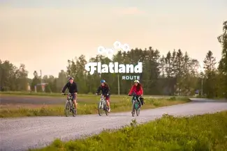 Kuva kolmesta pyöräilijästä soratiellä. Logo Flatland Route retkipyöräilyn rengasreitistä.