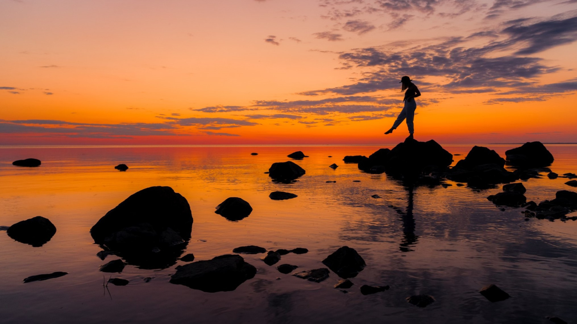 Henkilö tasapainottelemassa kivillä merenrannassa auringonlaskussa