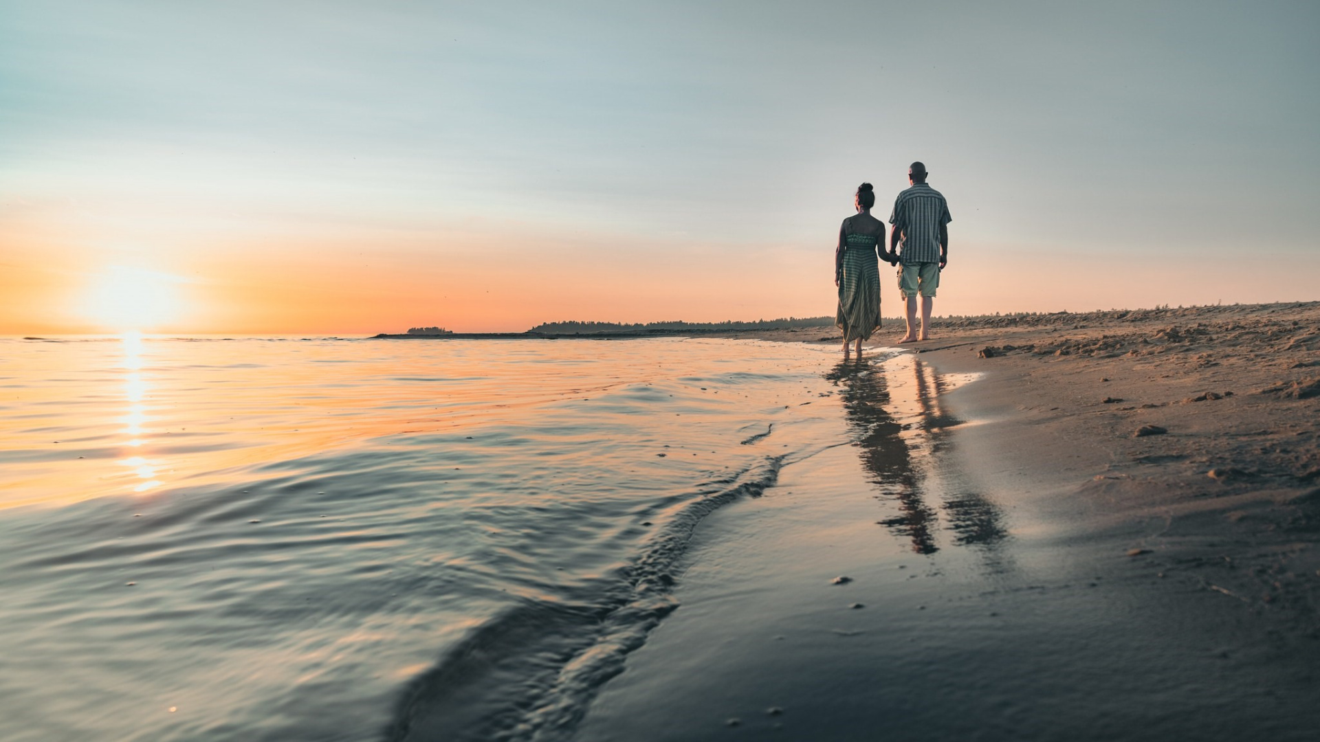 Pariskunta kävelee käsi kädessä meren rannalla auringonlaskussa